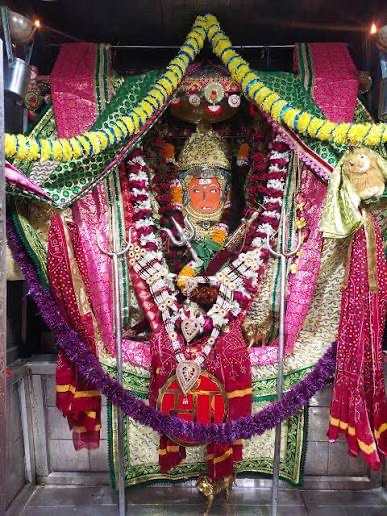Jeen Mata in full festival shringar with a green and pink chunari, yellow marigold toran, silver ornaments and a heart-shaped pendant